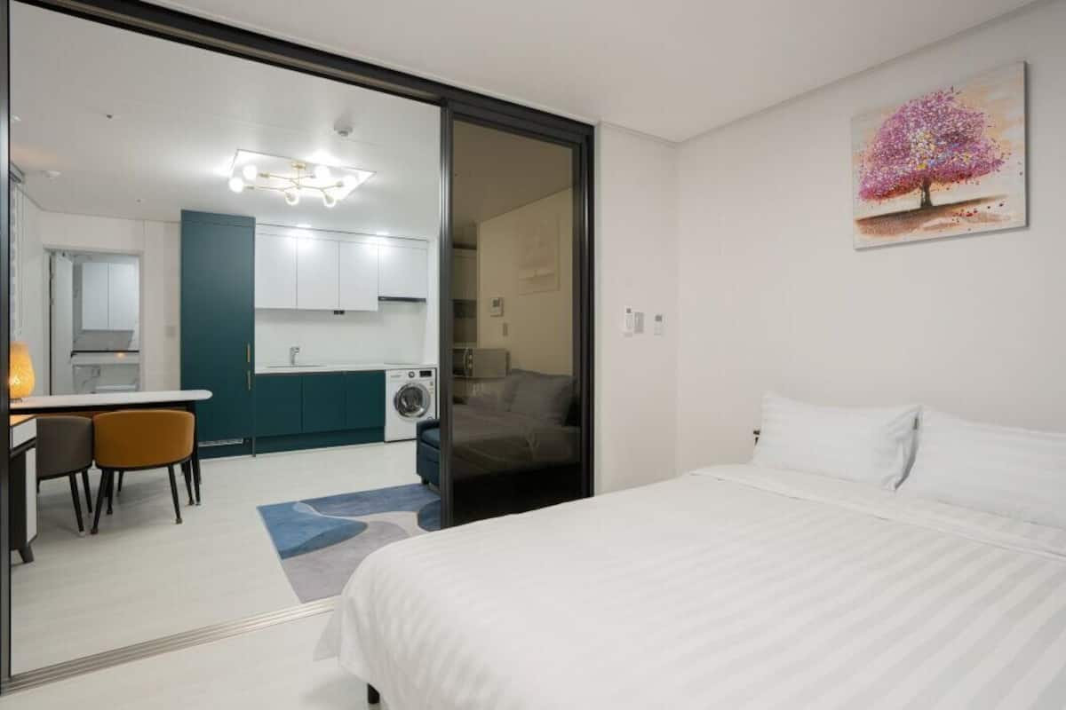 Une chambre d’hôtel moderne équipée d’un lit, d’un bureau avec des chaises, d’un lave-linge et d’une kitchenette.