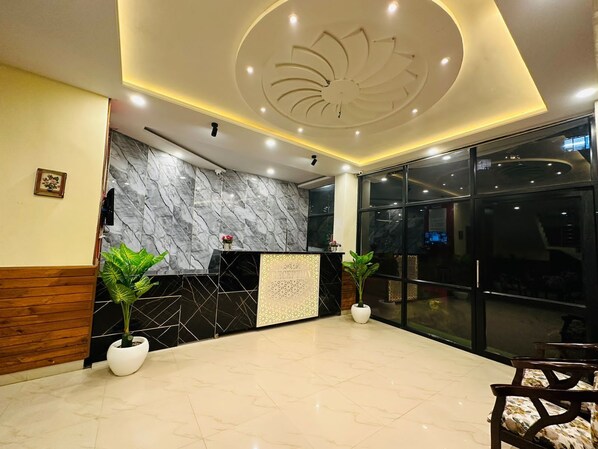 A modern reception area with a marble wall, a black and white patterned counter, and two potted plants.