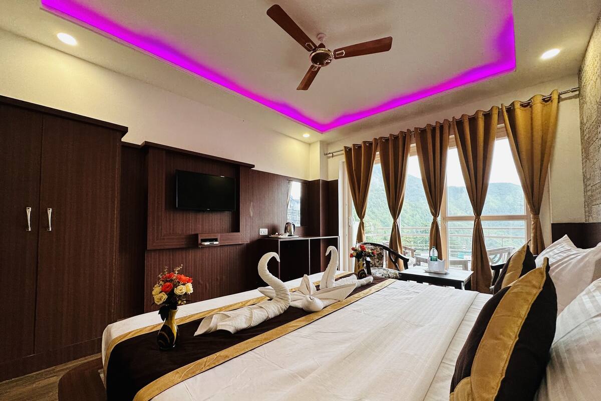 A hotel room with a bed, a flat-screen TV, a ceiling fan, and a view of the mountains.