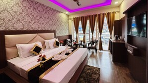Une chambre d’hôtel avec un grand lit, un ventilateur de plafond, une télévision et une vue sur la ville par les fenêtres.