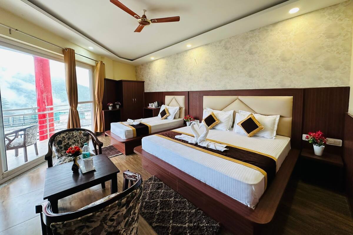 A hotel room with two beds, a dining table, a sofa, a ceiling fan, and a view of the outdoors.