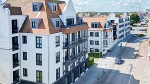 A row of modern apartment buildings with balconies, a paved street, and a car parked on the side. - Apartment in Cadzand-Bad | Duinhof V 1-7 (Cadzand)