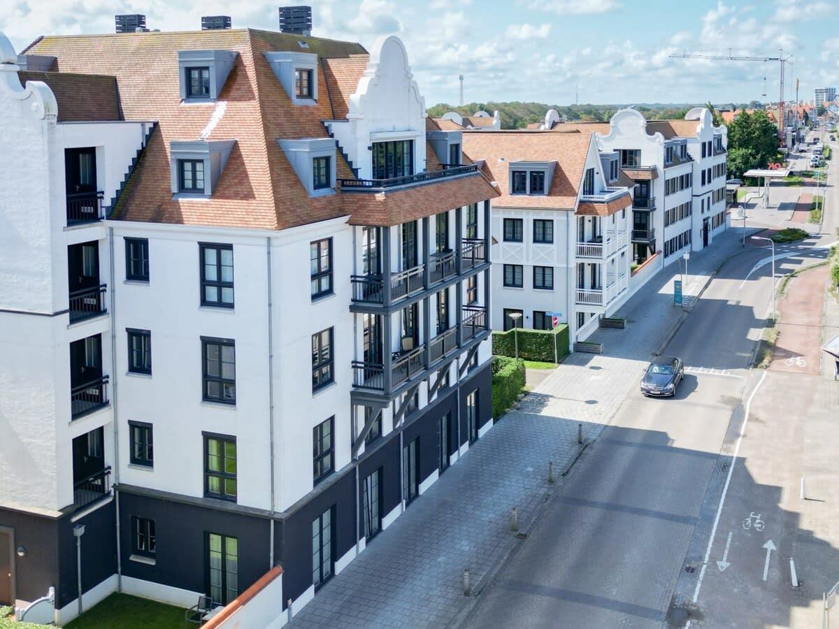 Une rangée d’immeubles d’appartements modernes dotés de balcons, une rue pavée et une voiture garée sur le bord.