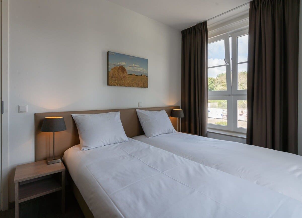A hotel room with two beds, a painting on the wall, and a window with curtains.