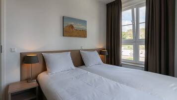 A hotel room with two beds, a painting on the wall, and a window with curtains.