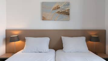 Ein Hotelzimmer mit zwei Betten, weißer Bettwäsche, einem Kopfteil und zwei Nachttischlampen.