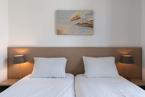 Habitación de hotel con dos camas individuales, ropa blanca y un cabecero con una obra de arte de espigas de trigo.