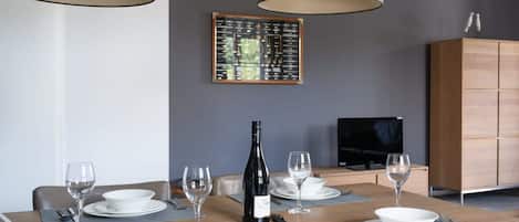 A dining area with a wooden table set for four, a bottle of wine, and a television in the background.