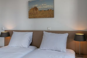 Une chambre d’hôtel avec deux lits, une tête de lit et un tableau accroché au mur représentant un champ avec des bottes de foin.