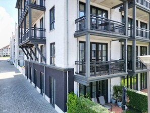 A multi-story building with balconies, a paved walkway, and greenery.