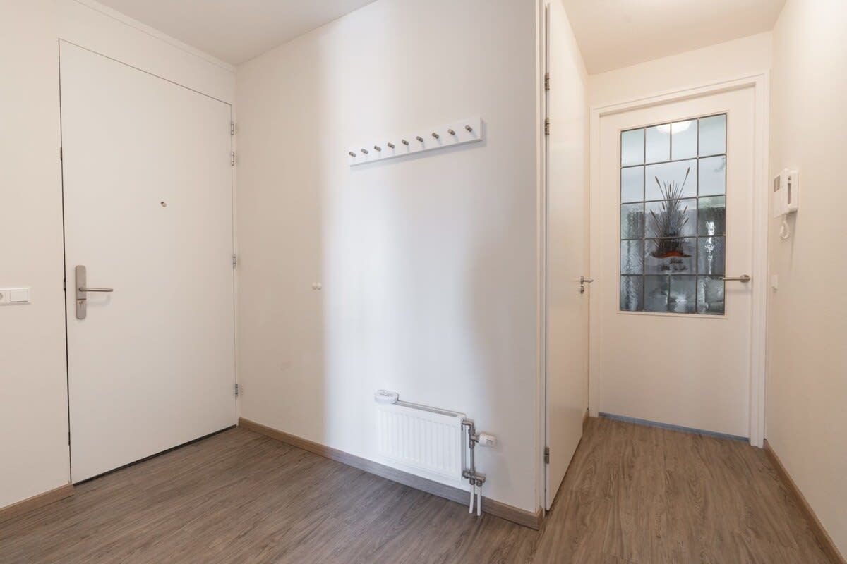 A hallway with a radiator, a coat rack, and a door with a window.