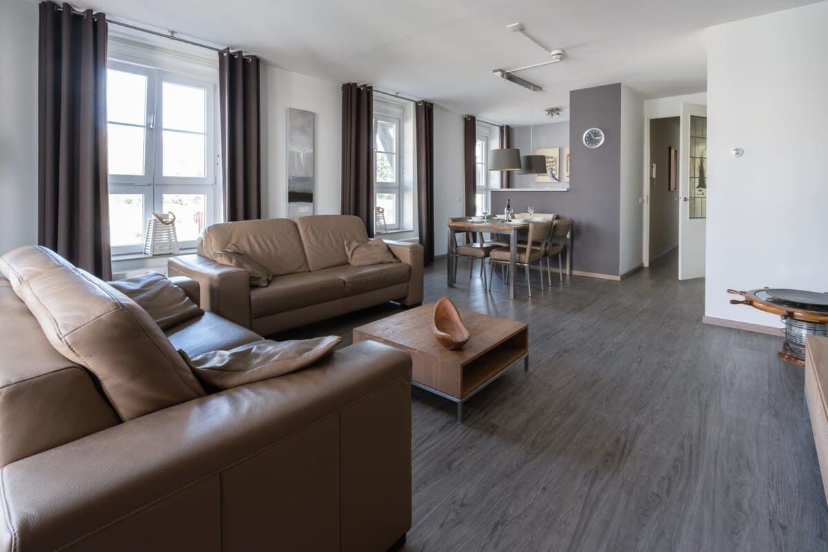 A modern living room with a sofa, a coffee table, and a dining area with chairs and a table.