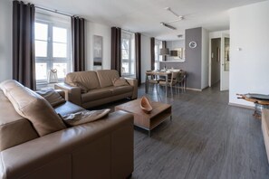 A modern living room with a sofa, a dining table, and a kitchen area in the background.