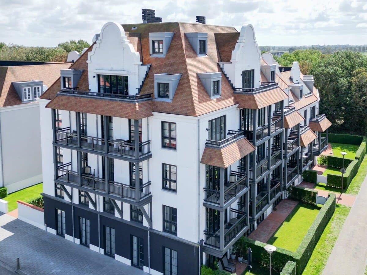A multi-story residential building with a modern architectural design, featuring balconies and a well-maintained garden.
