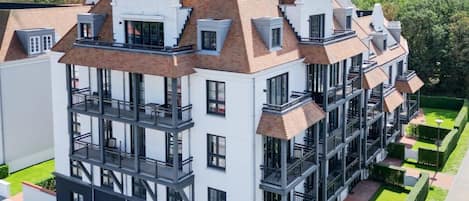 Un edificio residencial de varios pisos con un diseño arquitectónico moderno, con balcones y un jardín bien cuidado.