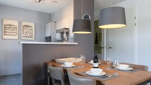 A dining area with a wooden table set for four, two pendant lights, a white cabinet with kitchen appliances, and artwork on the wall. - Apartment in Cadzand-Bad | Duinhof V 1-7 (Cadzand)