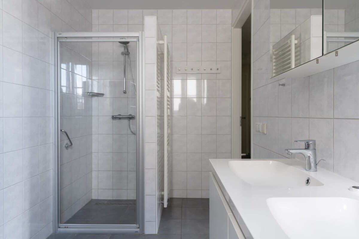Ein modernes Badezimmer mit einer Duschkabine aus Glas, einem weißen Waschbecken und einem Spiegel.