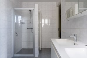 Une salle de bain moderne avec une douche à parois de verre, un lavabo blanc et un miroir.