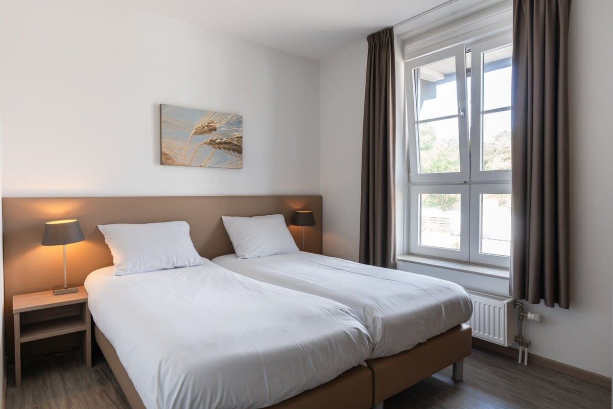 Een hotelkamer met een tweepersoonsbed, nachtlampjes, een raam met gordijnen en een kunstwerk aan de wand.