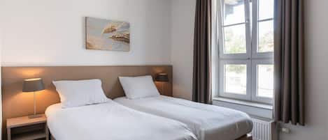 A hotel room with a double bed, bedside lamps, a window with curtains, and a wall-mounted artwork.
