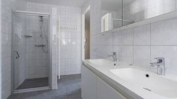 Une salle de bain moderne avec une douche à parois de verre, un double vasque et un grand miroir.