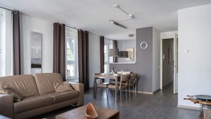A modern living room with a sofa, coffee table, and dining area. - Apartment in Cadzand-Bad | Duinhof V 1-7 (Cadzand)