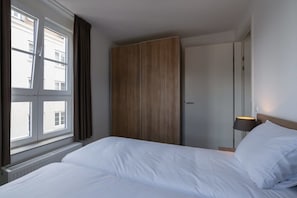 Une chambre d’hôtel avec un lit, une armoire, une fenêtre avec des rideaux et une lampe de chevet.