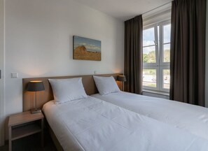 Une chambre d’hôtel avec deux lits, un tableau au mur et une fenêtre avec des rideaux.