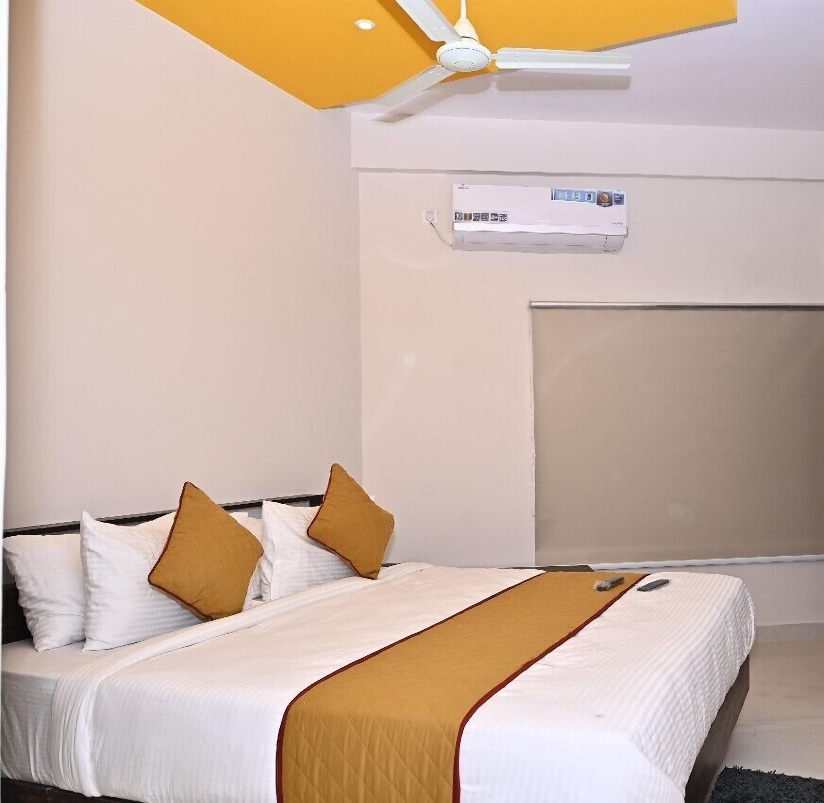 A hotel room with a bed, a ceiling fan, an air conditioning unit, and a large window.
