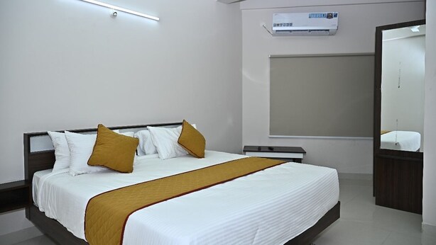 A modern hotel room with a large bed, a bedside table, a nightstand, a wall-mounted air conditioner, and a mirror. - Hotel SLN Comfort (Tumkur)