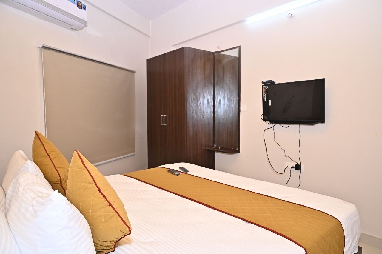 A hotel room with a bed, a wardrobe, a television mounted on the wall, and an air conditioning unit above the bed.