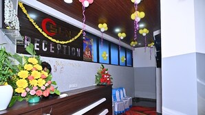 A reception area with a wooden reception desk, a floral arrangement, and a wall-mounted sign. - Hotel SLN Comfort (Tumkur)