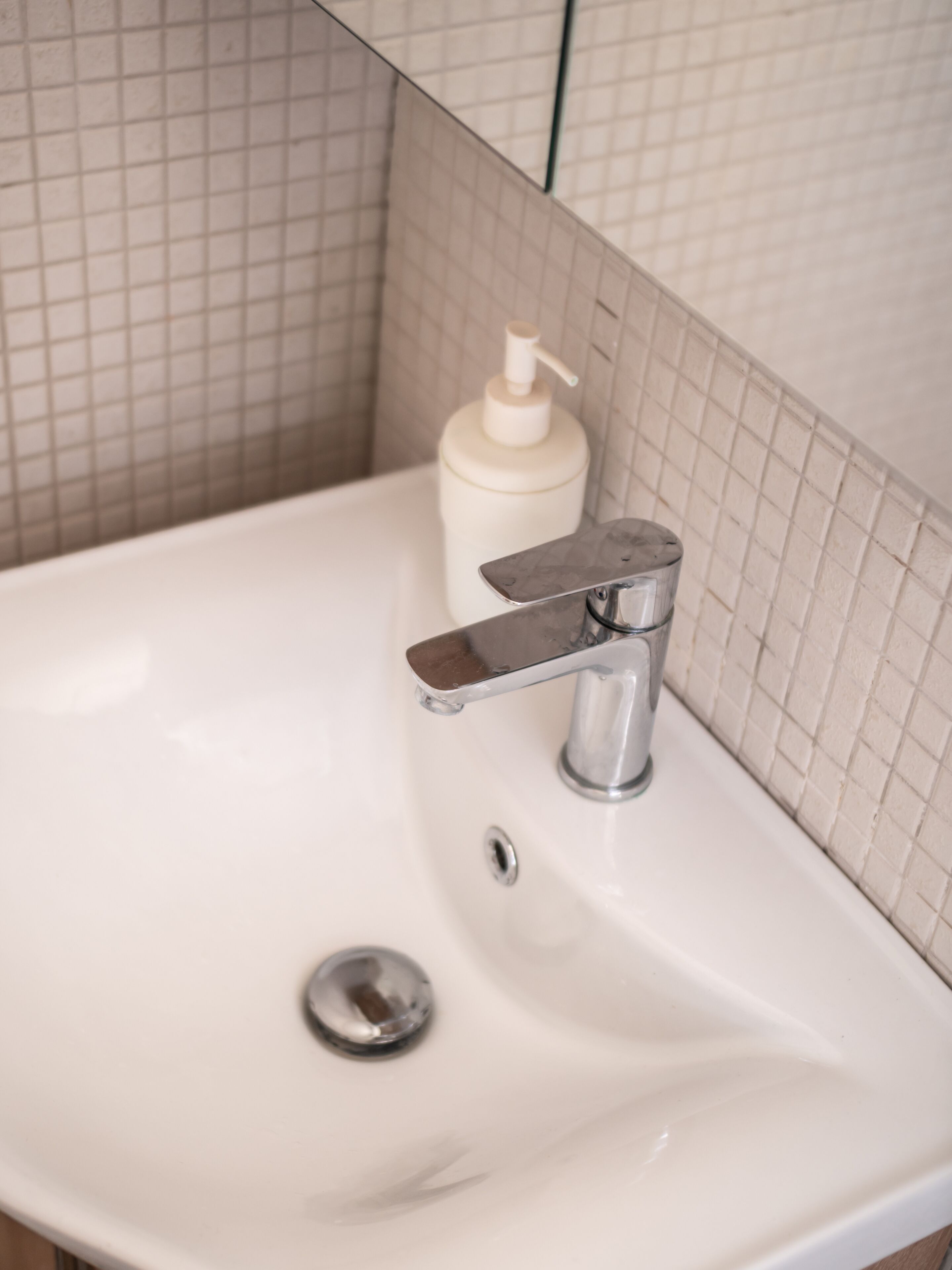 A bathroom sink with a chrome faucet, a soap dispenser, and a drain.