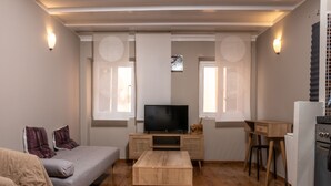 A compact living space with a sofa, a TV, a wooden coffee table, a small kitchen area, and a dining table. - CAMPIELLO Apt. by LOC HOSPITALITY (Corfu)