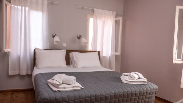 A neatly made bed with a grey quilt, white pillows, and folded towels on a wooden floor. - CAMPIELLO Apt. by LOC HOSPITALITY (Corfu)