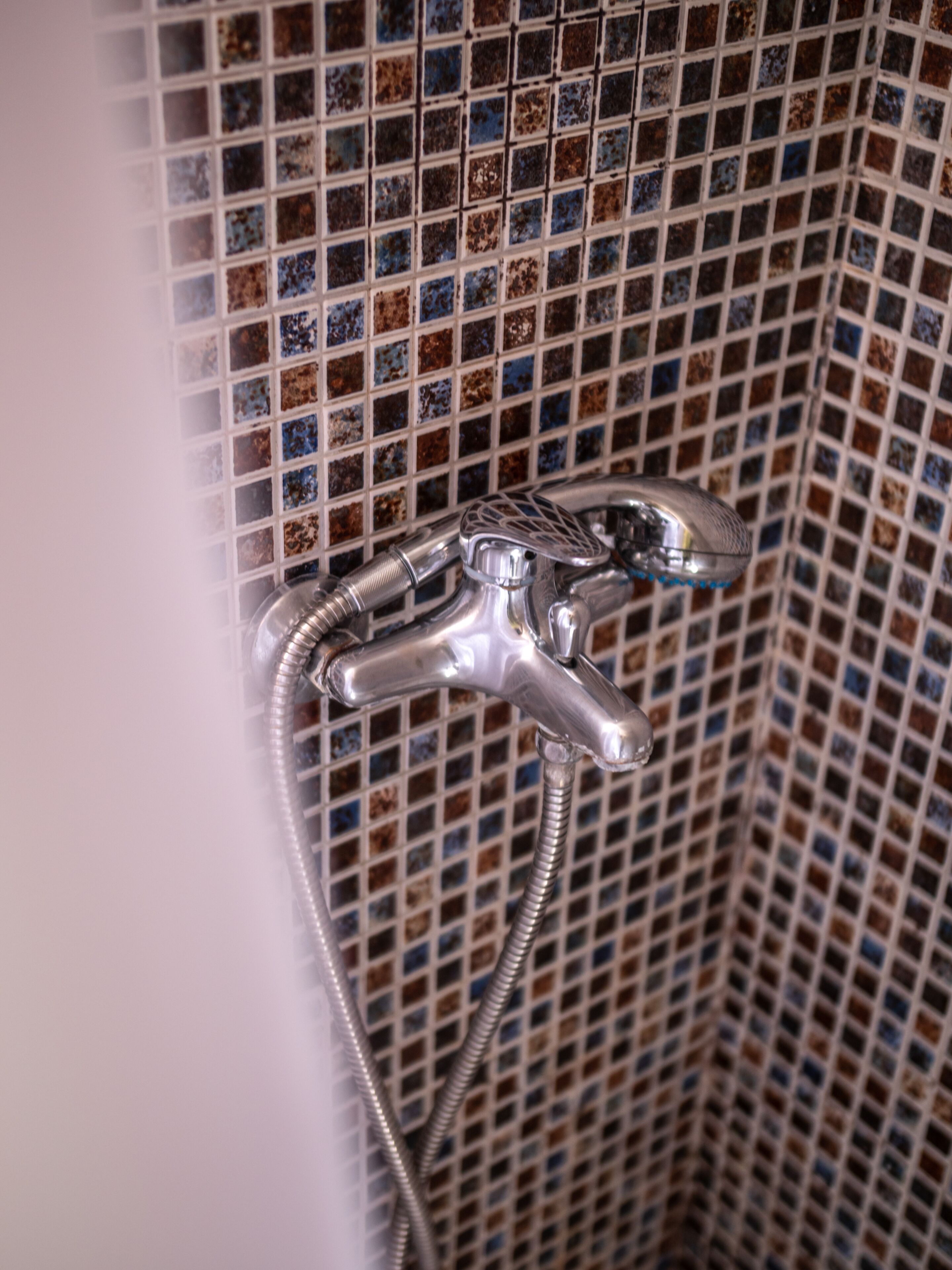 Een badkamer met een betegelde douchewand en een verchroomde douchekop met een flexibele slang.