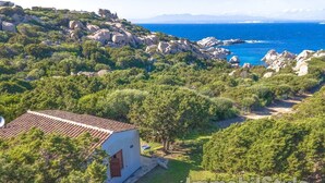 A small white building with a red roof, surrounded by lush greenery and rocky terrain, overlooking a coastal area. - Bungalow D'elite a Capo Testa (Capo Testa)