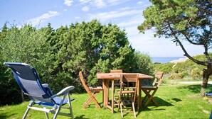 A wooden table and chairs set on a grassy lawn with a clear sky and trees in the background. - Bungalow D'elite a Capo Testa (Capo Testa)