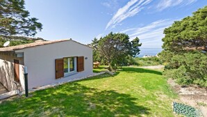 A single-story house with a white exterior and brown shutters, a small garden, and a view of the sea. - Bungalow D'elite a Capo Testa (Capo Testa)