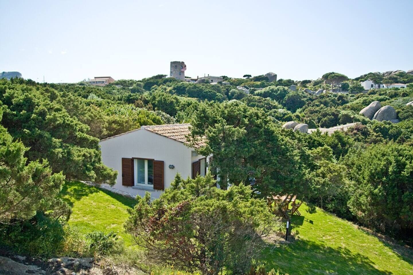 Uma casa pequena e moderna, rodeada por vegetação exuberante e terreno rochoso.