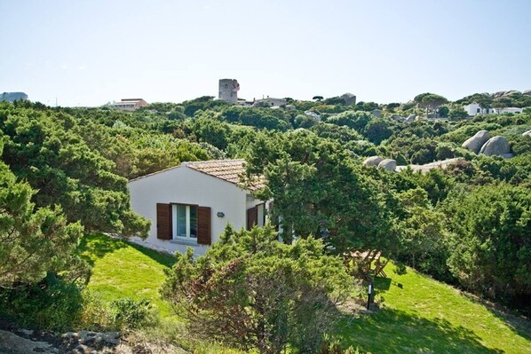 A small, modern house surrounded by lush greenery and rocky terrain.