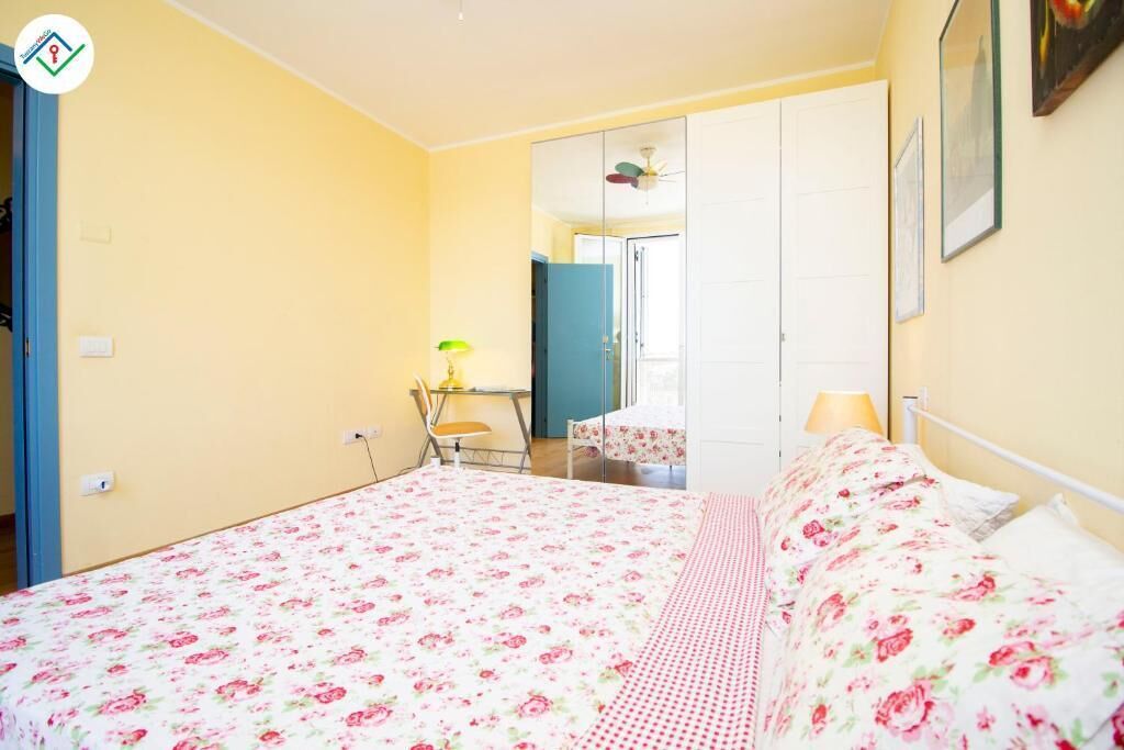 Une chambre à coucher avec une couvre-lit à motifs floraux, un bureau avec une lampe et une armoire.