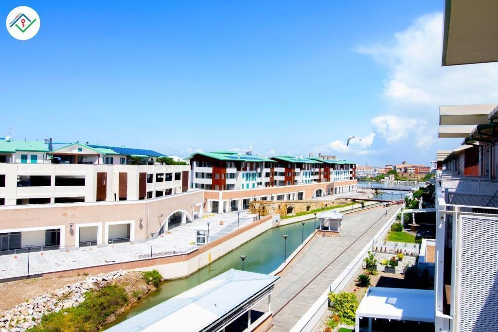A modern building with multiple floors, a canal running through the middle, and a bridge in the background.