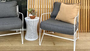 A modern outdoor seating area with two grey chairs and a small round table with a potted plant.