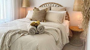 A neatly made bed with rolled towels, a ceiling fan, and a wall-mounted air conditioner.