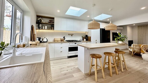 A modern kitchen with a central island, wooden stools, and pendant lighting.