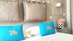 A hotel room with a bed, two pillows with a sea turtle design, a nightstand with a vase of flowers, and a wall-mounted light. - Villa Antonietta Ischia  (Forio)