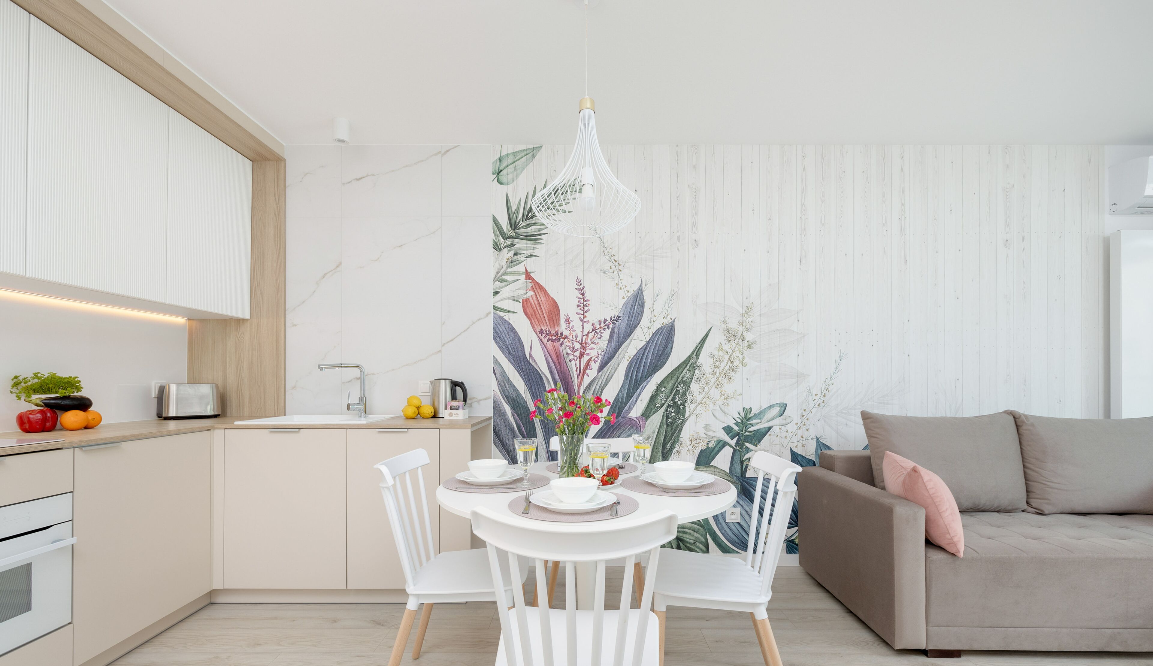 Una cocina moderna con armarios blancos, un comedor con mesa y sillas blancas, y una sala de estar con sofá.