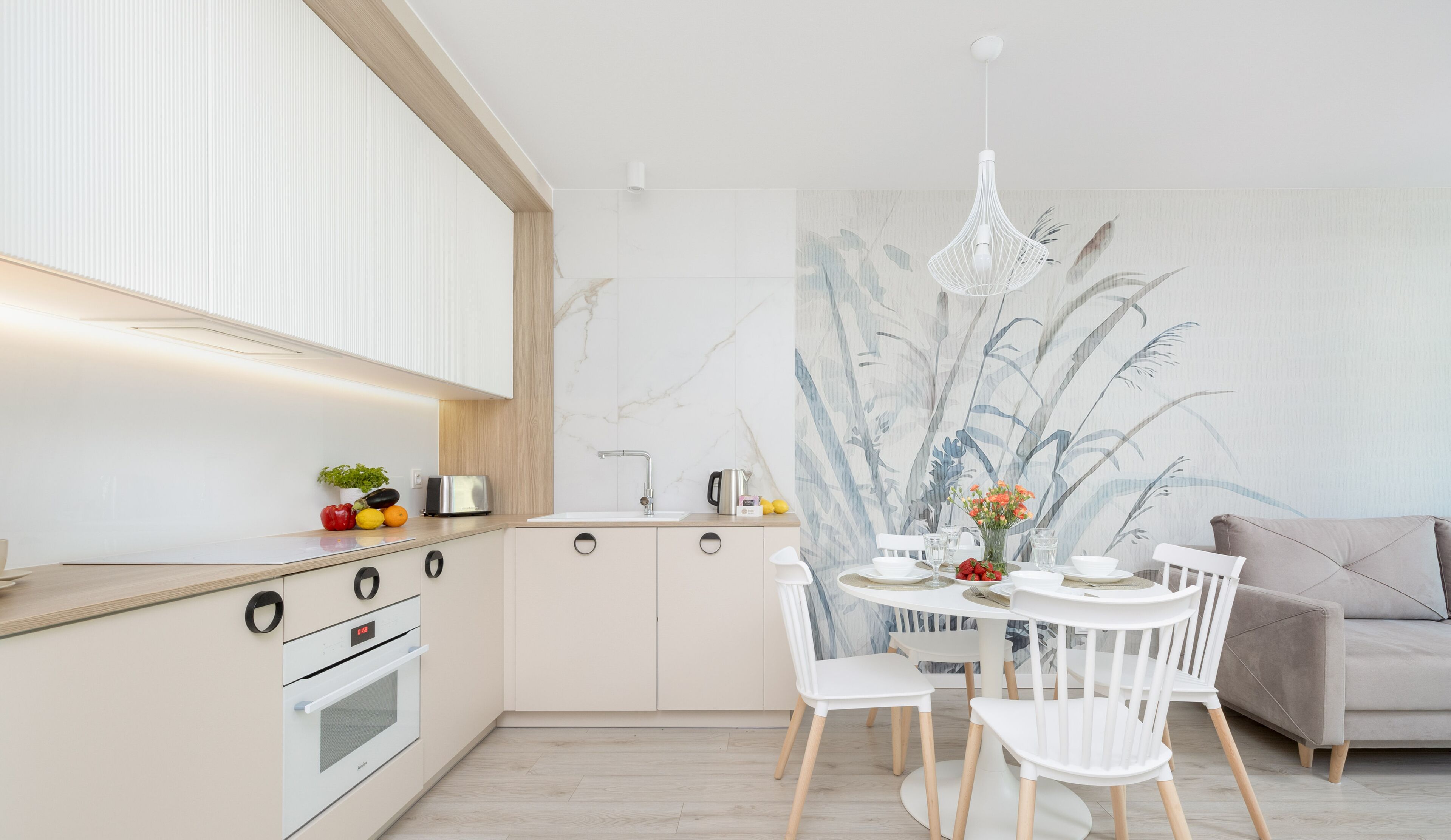 Una cocina moderna con comedor, que presenta una paleta de colores blanco y madera clara, un ventanal grande y un mural en la pared.