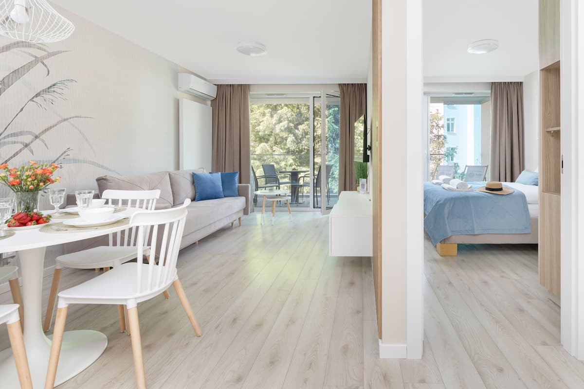 Ett modernt hotellrum med en matplats, en soffa, en säng och en balkong med utsikt över träd.